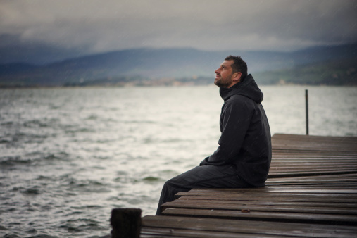 Lonely man sitting on pier under rain